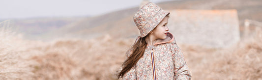 Une petite fille avec un coupe vent et un chapeau K-Way regarde au loin