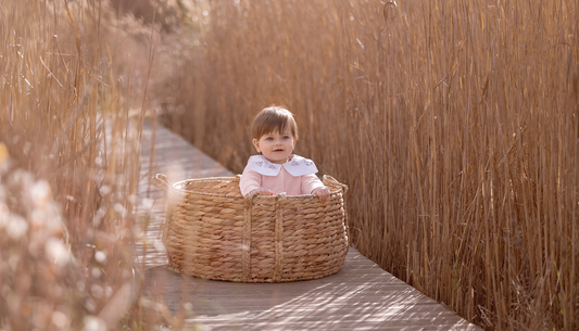 Bébé porte une combinaison rose dans un panier en osier 